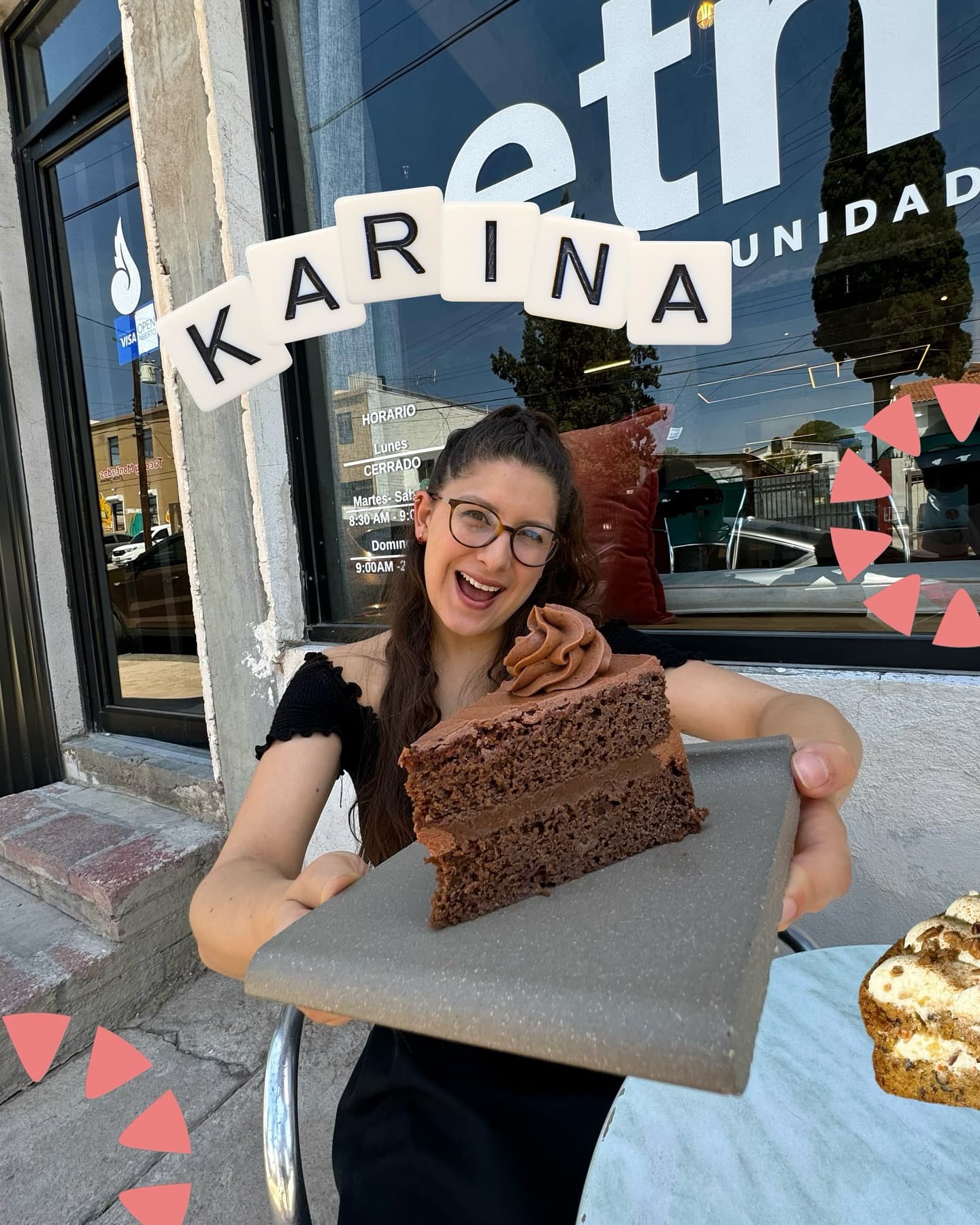 Karina, de Kiki The Cake Shop, sosteniendo una rebanada de pastel de chocolate frente a Café Etnos