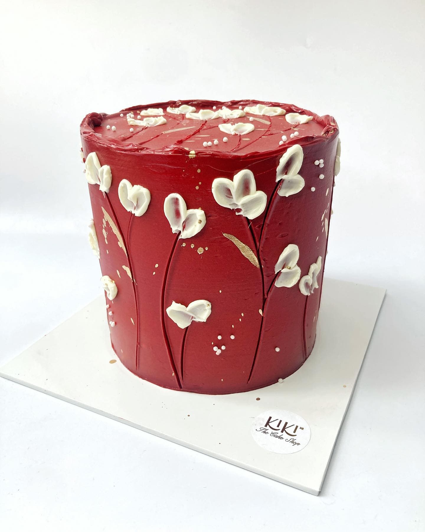 Pastel rojo con flores blancas de betún y detalles en hoja de oro