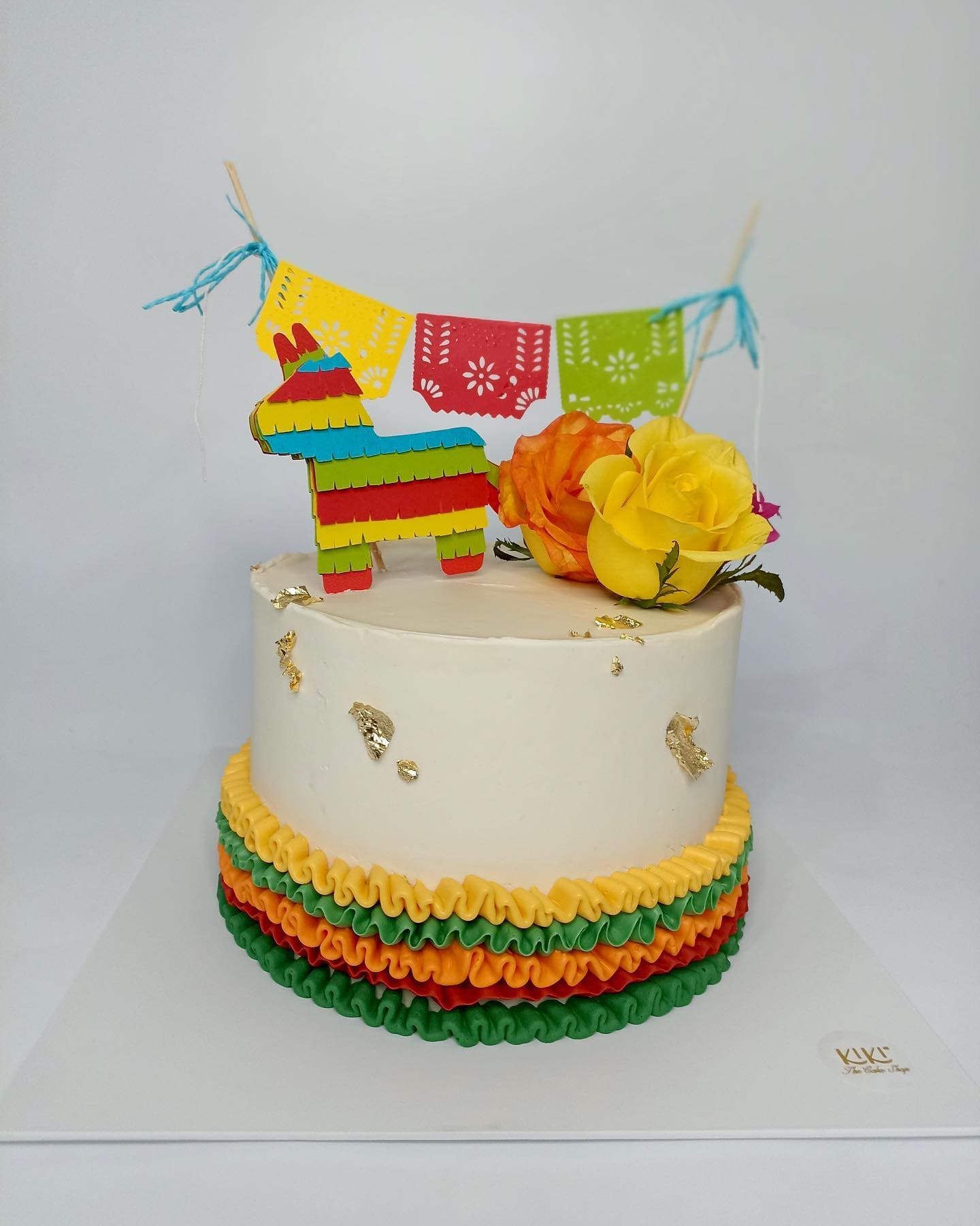 Pastel blanco con base de holanes de colores, piñata y papel picado